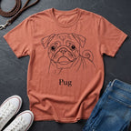 Coral t-shirt with a pug design and 'Pug' text, placed on a dark surface with shoes and jeans.