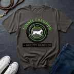 Beige t-shirt with 'Tunnel Champion Agility Handler' graphic on a dark surface with shoes and jeans.