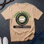Beige t-shirt with 'Tunnel Champion Agility Handler' graphic on a dark surface with shoes and jeans.