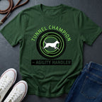 Beige t-shirt with 'Tunnel Champion Agility Handler' graphic on a dark surface with shoes and jeans.