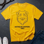 Yellow Comfort Colors t-shirt with Australian Shepherd design and text on a dark surface with shoes and jeans.