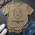 Beige Comfort Colors t-shirt with Australian Shepherd design and text on a dark surface with shoes and jeans.