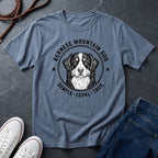 Blue Comfort Colors t-shirt with Bernese Mountain Dog graphic and text on a dark surface with shoes and jeans.