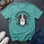 Teal Comfort Colors t-shirt with Bernese Mountain Dog graphic and text on a dark surface with shoes and jeans.