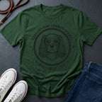 Green Comfort Colors t-shirt with Australian Shepherd graphic and text on a dark surface with shoes and jeans.