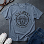 Blue Comfort Colors t-shirt with Dachshund graphic and text on a dark surface with shoes and jeans.