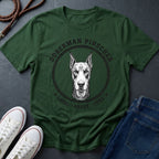 Green Comfort Colors t-shirt with Doberman Pinscher graphic and text on a dark surface with shoes and jeans.