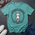 Teal Comfort Colors t-shirt with Doberman Pinscher graphic and text on a dark surface with shoes and jeans.
