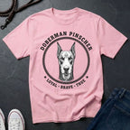 Pink Comfort Colors t-shirt with Doberman Pinscher graphic and text on a dark surface