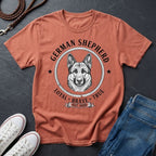 Coral Comfort Colors t-shirt with German Shepherd graphic and text on a dark surface with shoes and jeans.