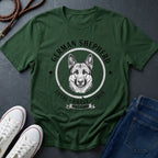 Green Comfort Colors t-shirt with German Shepherd graphic and text on a dark surface with shoes and jeans.