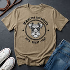 Beige Comfort Colors t-shirt with miniature schnauzer graphic and text on a dark surface with shoes and jeans.