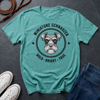 Teal Comfort Colors t-shirt with miniature schnauzer graphic and text on a dark surface with shoes and jeans.