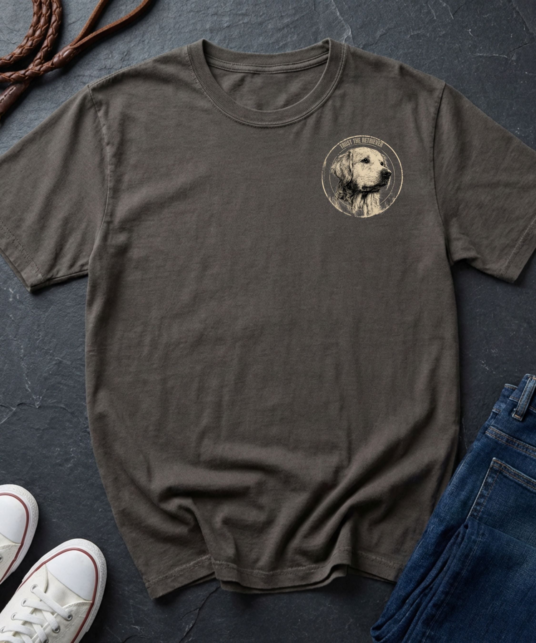 Brown Comfort Colors t-shirt with a dog graphic on a dark surface with shoes and jeans.