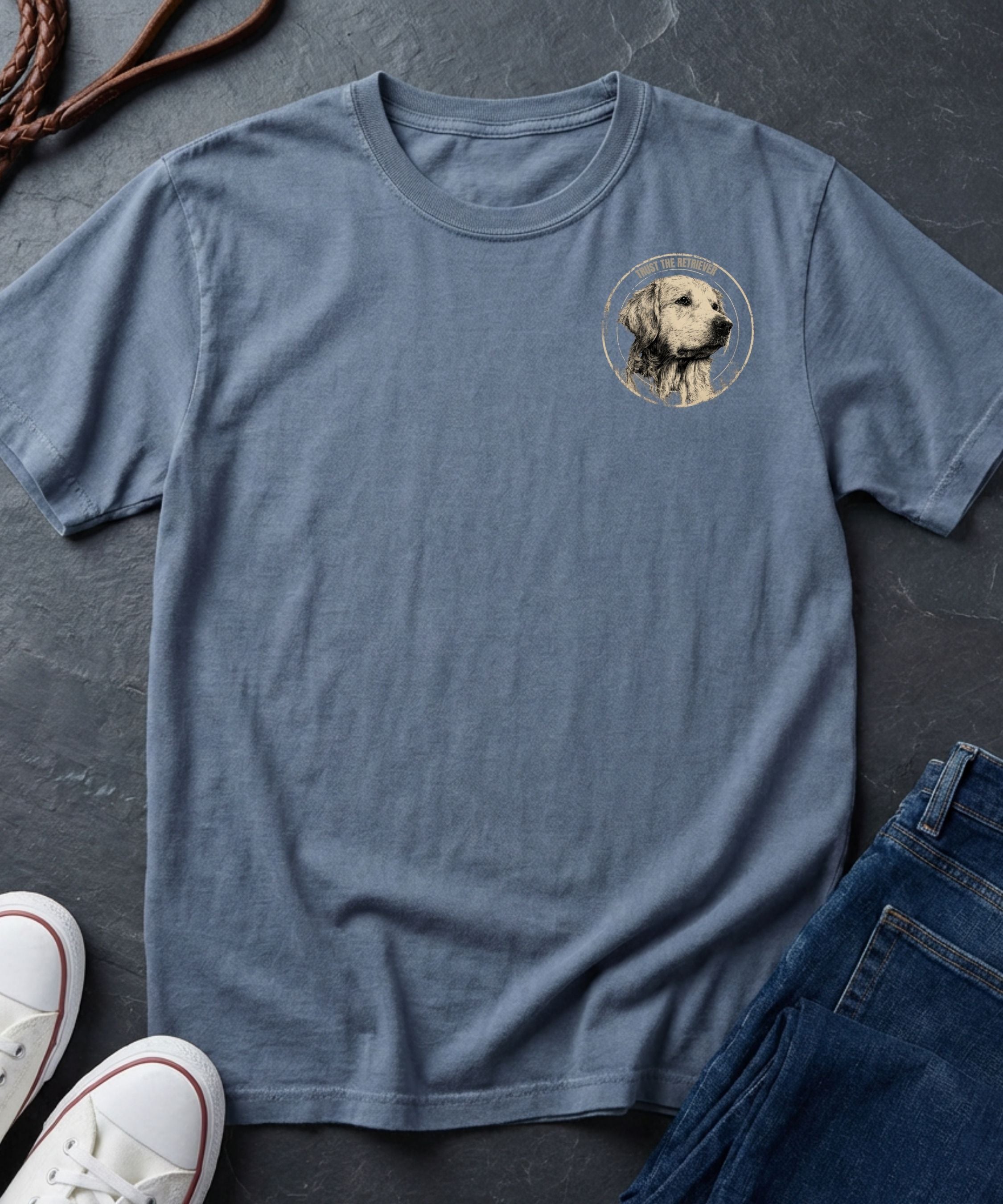 Blue Comfort Colors t-shirt with a dog graphic on a dark surface with shoes and jeans.