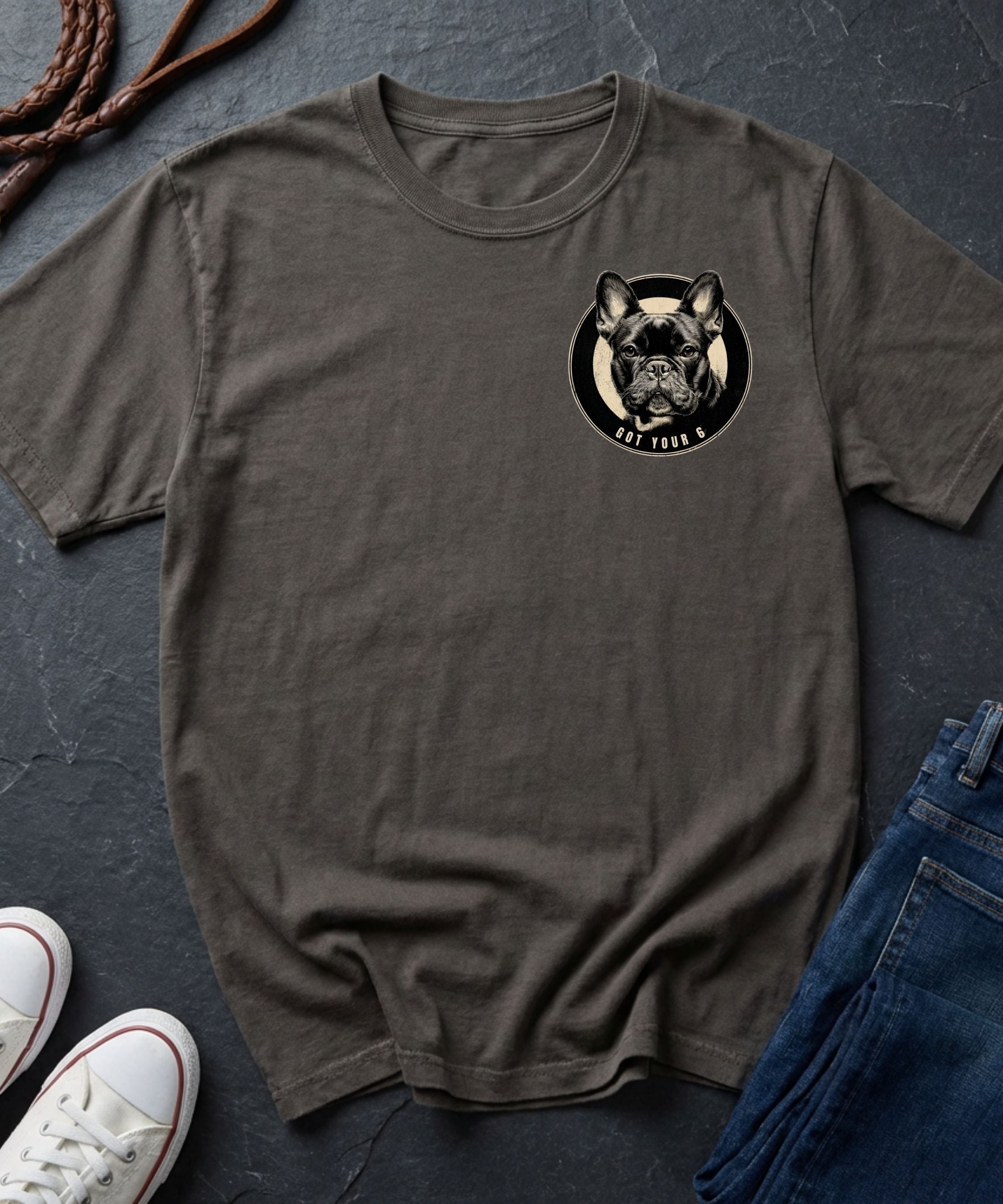 Brown Comfort Colors t-shirt with a dog graphic on a dark surface with shoes and jeans.