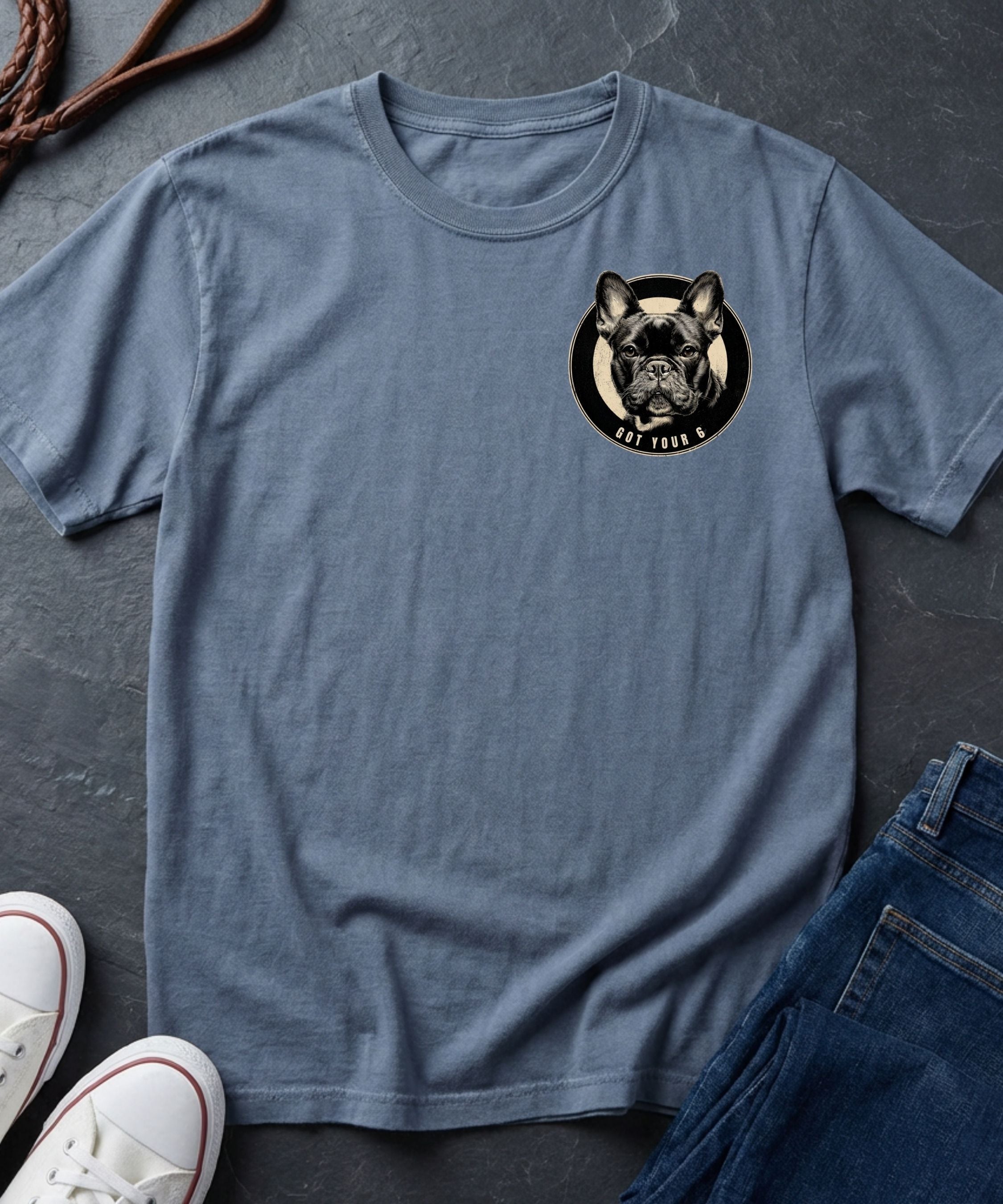 Blue Comfort Colors t-shirt with a dog graphic on a dark surface with shoes and jeans.