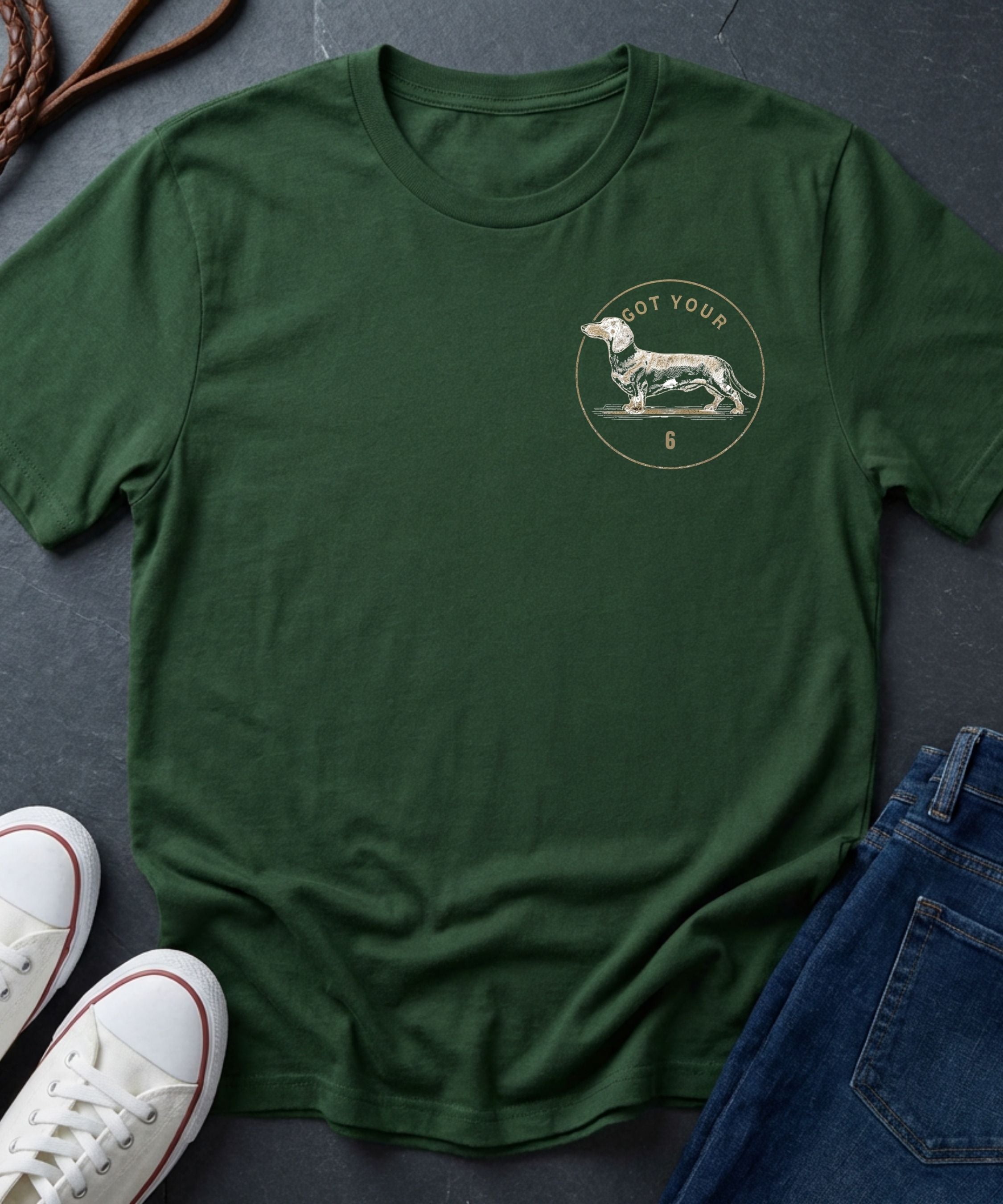 Green Comfort Colors t-shirt with a dog graphic and text on a dark surface with shoes and jeans.
