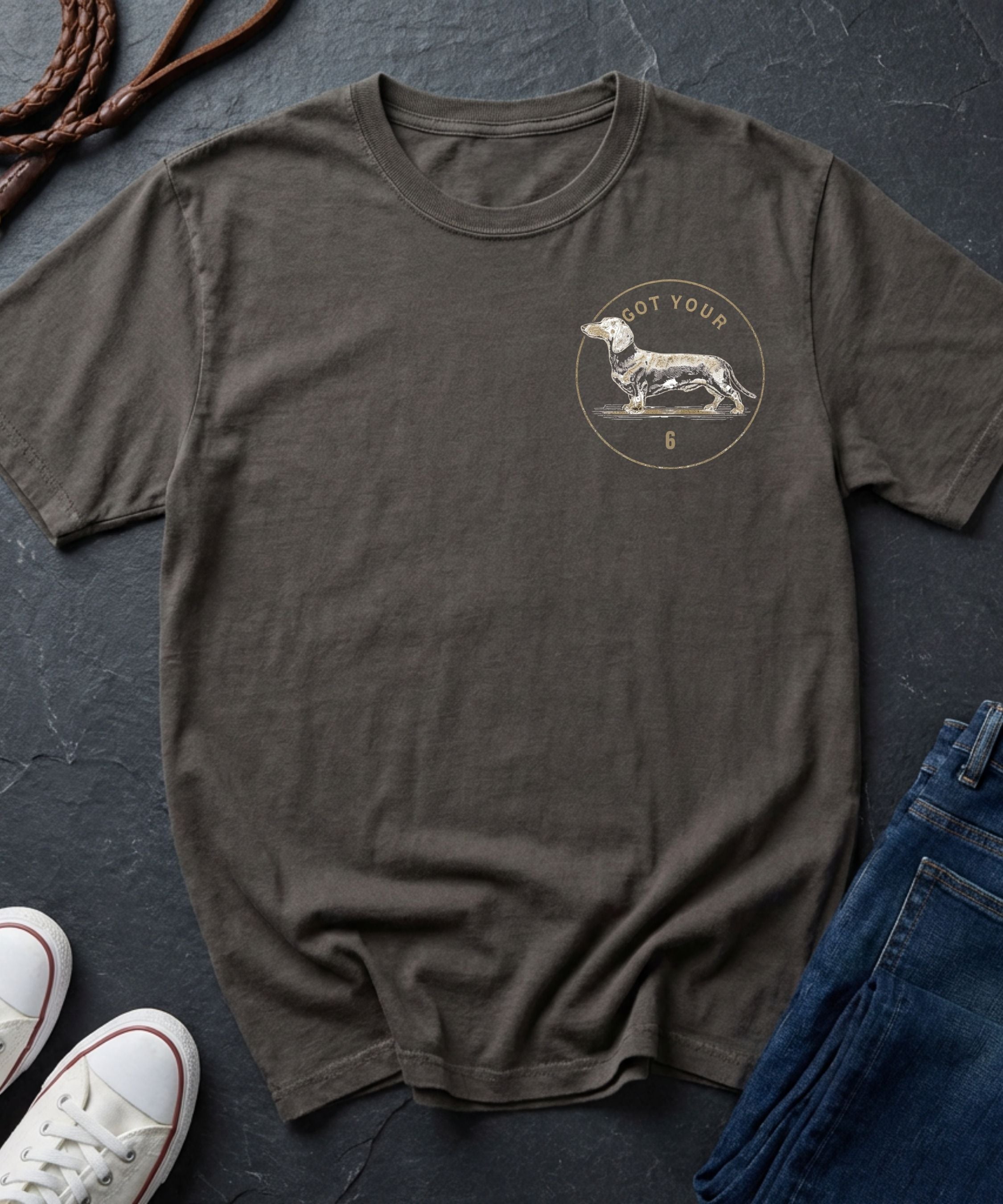 Brown Comfort Colors t-shirt with a dog graphic on a dark surface with shoes and jeans.