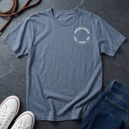 Blue Comfort Colors t-shirt with a logo on a dark surface with shoes and jeans.