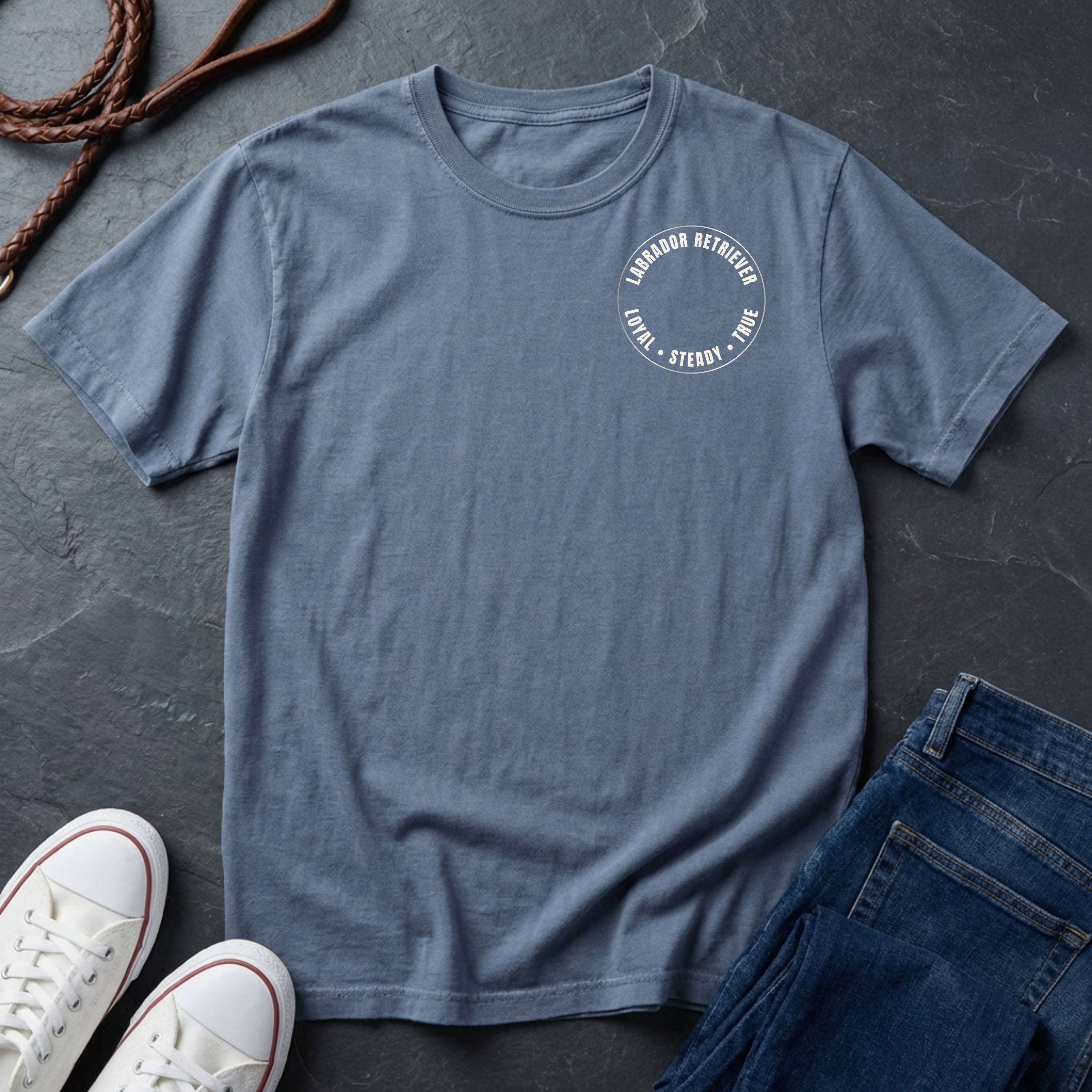 Blue Comfort Colors t-shirt with a logo on a dark surface with shoes and jeans.