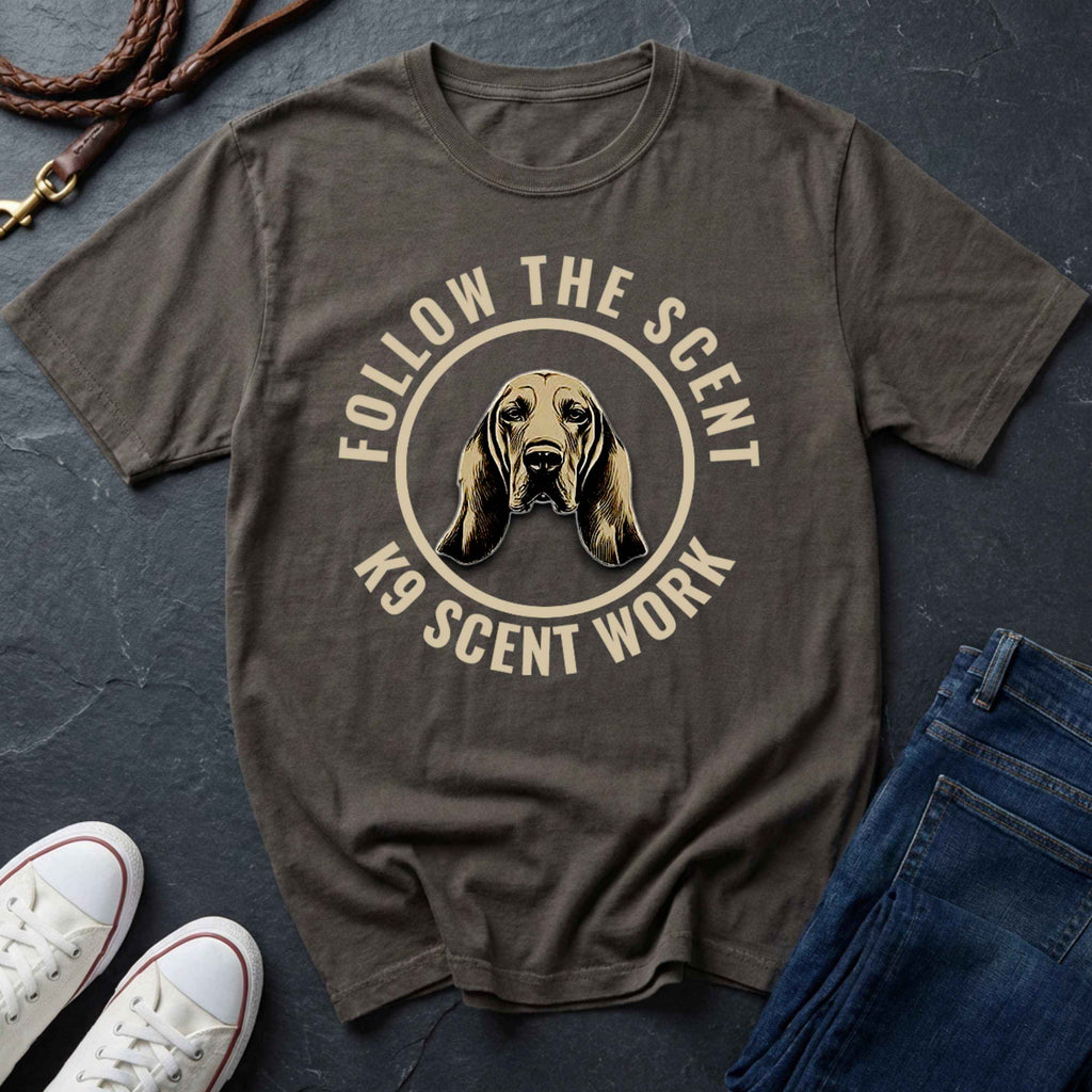 Gray Comfort Colors t-shirt with a dog graphic and text 'Follow the Scent K9 Scent Work' on a dark surface with shoes and jeans.