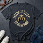 Navy blue Comfort Colors t-shirt with a dog graphic and text 'Follow the Scent K9 Scent Work' on a dark surface with shoes and jeans.