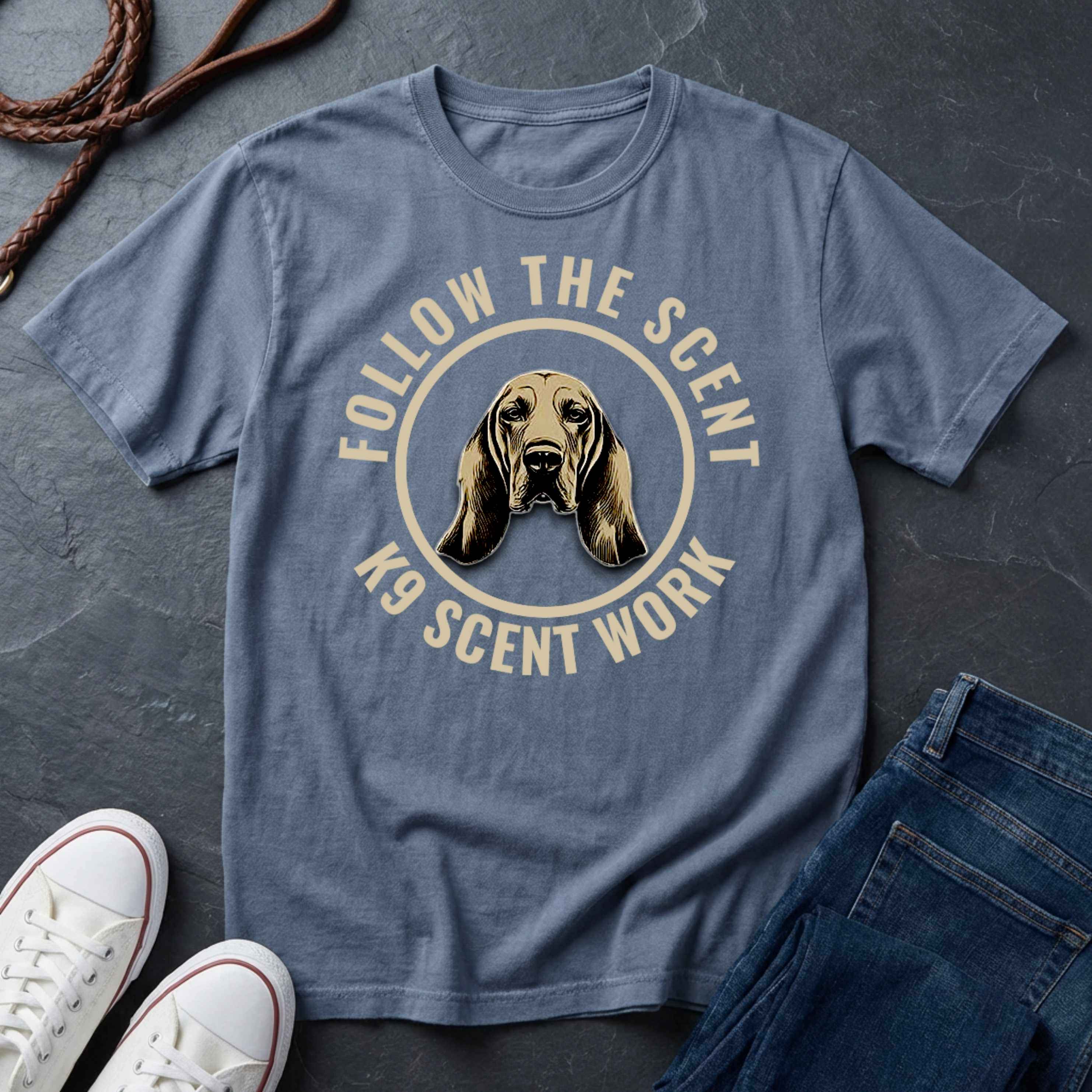 Blue Comfort Colors t-shirt with a dog graphic and text 'Follow the Scent K9 Scent Work' on a dark surface with shoes and jeans.