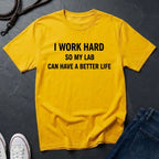 Yellow Comfort Colors t-shirt with text 'I work hard so my lab can have a better life' on a dark surface.