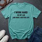 Teal Comfort Colors  t-shirt with 'I work hard so my lab can have a better life' text on a dark surface with shoes and jeans.
