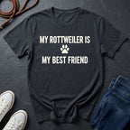 Black Comfort Colors t-shirt with 'My Rottweiler is my best friend' text on a dark surface with shoes and jeans.