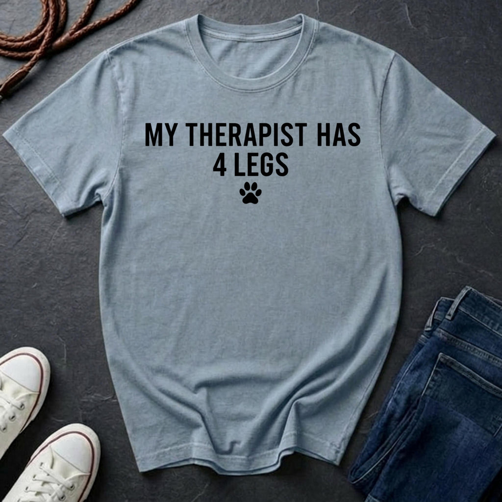 Light blue Comfort Colors t-shirt with 'My therapist has 4 legs' text on a dark surface with shoes and jeans.