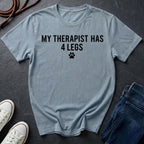 Light blue Comfort Colors t-shirt with 'My therapist has 4 legs' text on a dark surface with shoes and jeans.