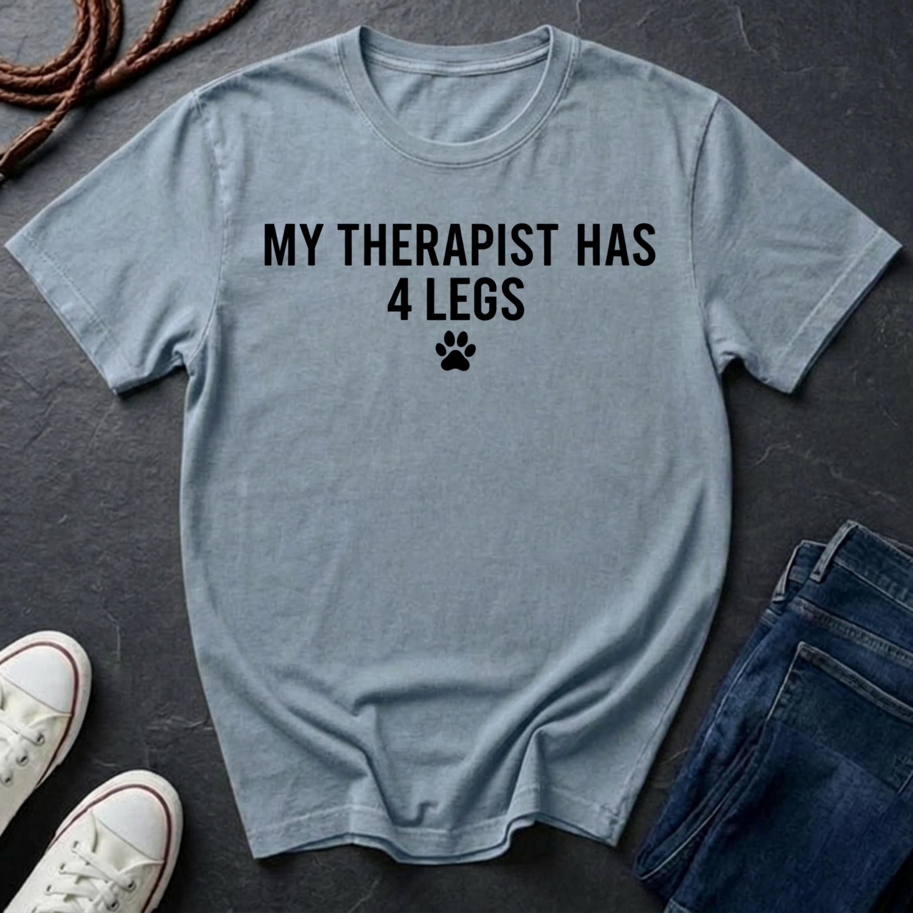 Light blue Comfort Colors t-shirt with 'My therapist has 4 legs' text on a dark surface with shoes and jeans.