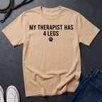 Beige Comfort Colors t-shirt with 'My therapist has 4 legs' text on a dark surface with jeans and shoes.