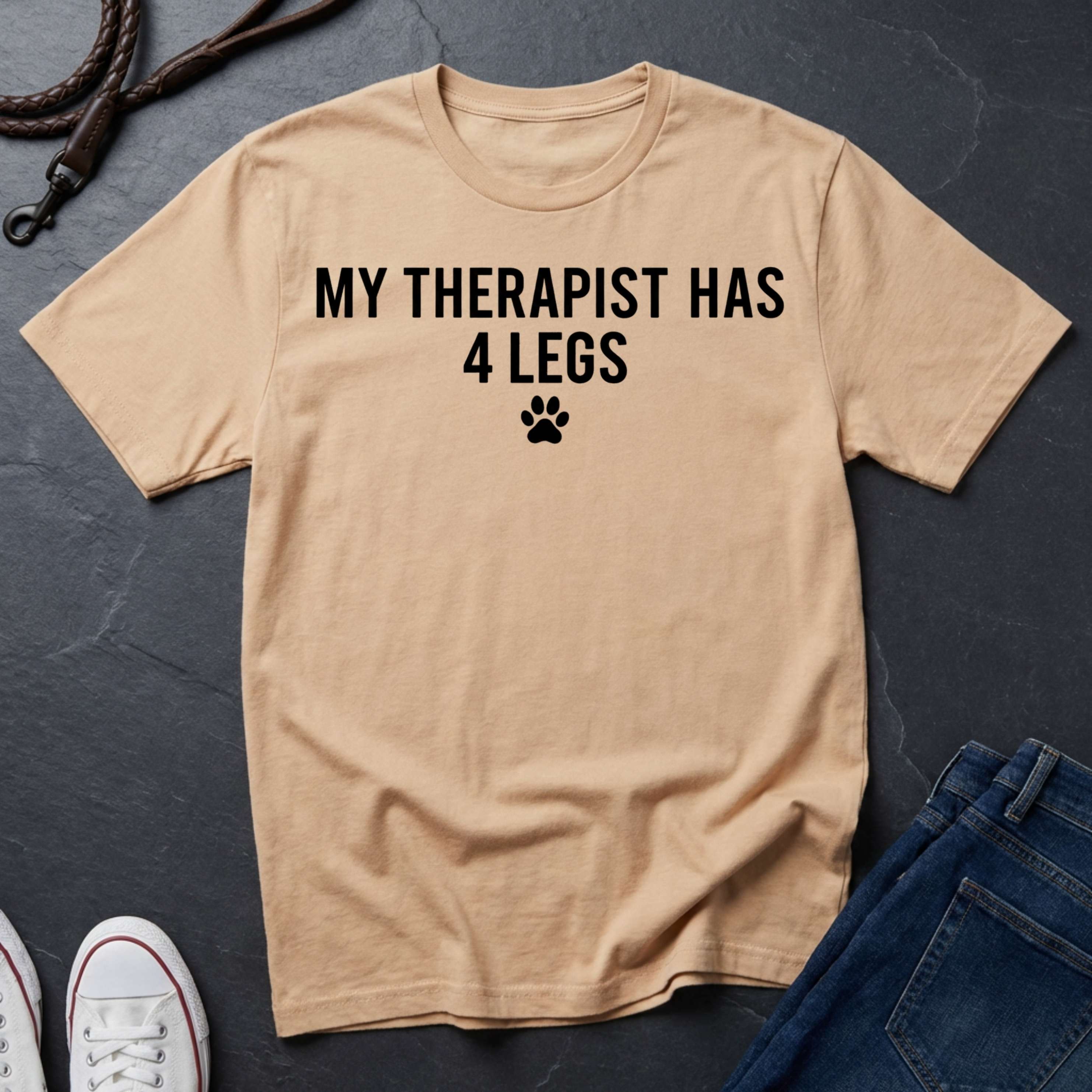 Beige Comfort Colors t-shirt with 'My therapist has 4 legs' text on a dark surface with jeans and shoes.