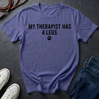 Purple Comfort Colors t-shirt with 'My therapist has 4 legs' text on a dark surface with shoes and jeans.