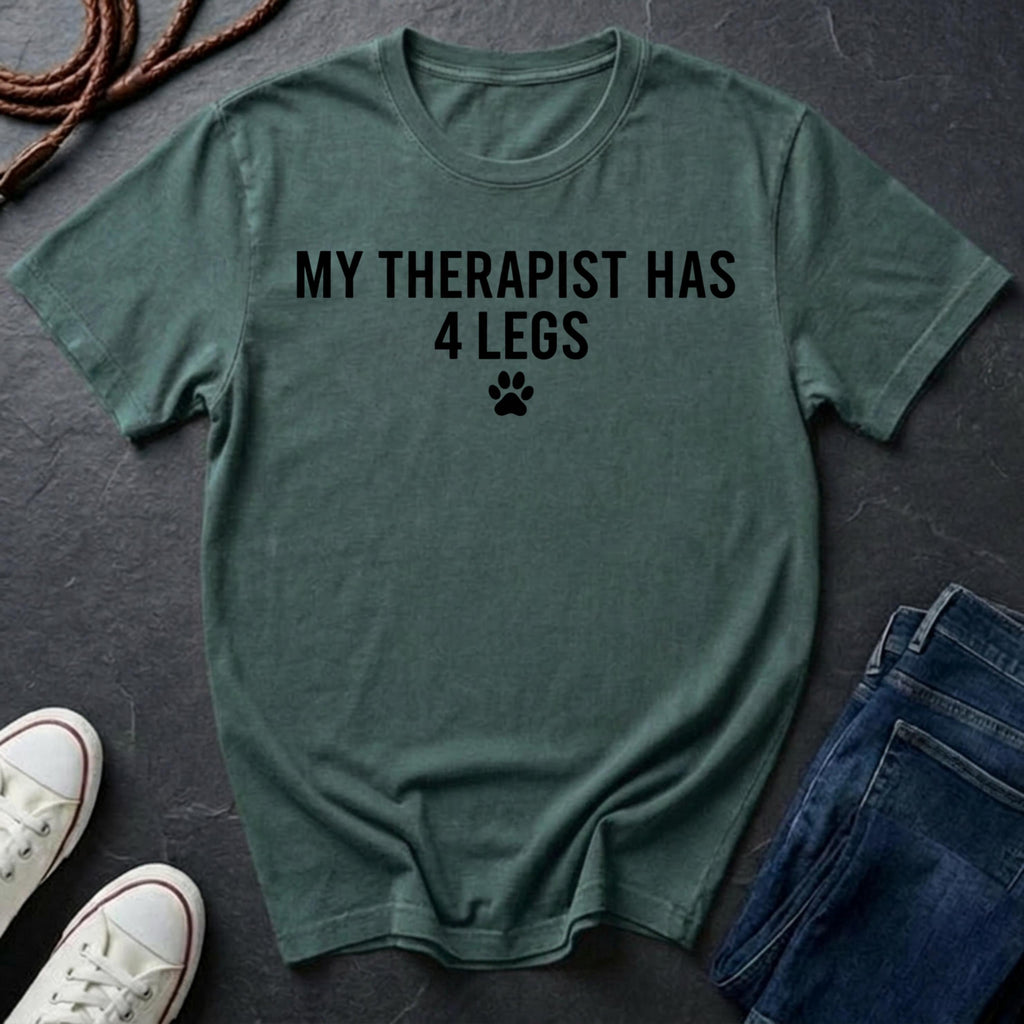 Green Comfort Colors t-shirt with 'My therapist has 4 legs' text on a dark surface with shoes and jeans.