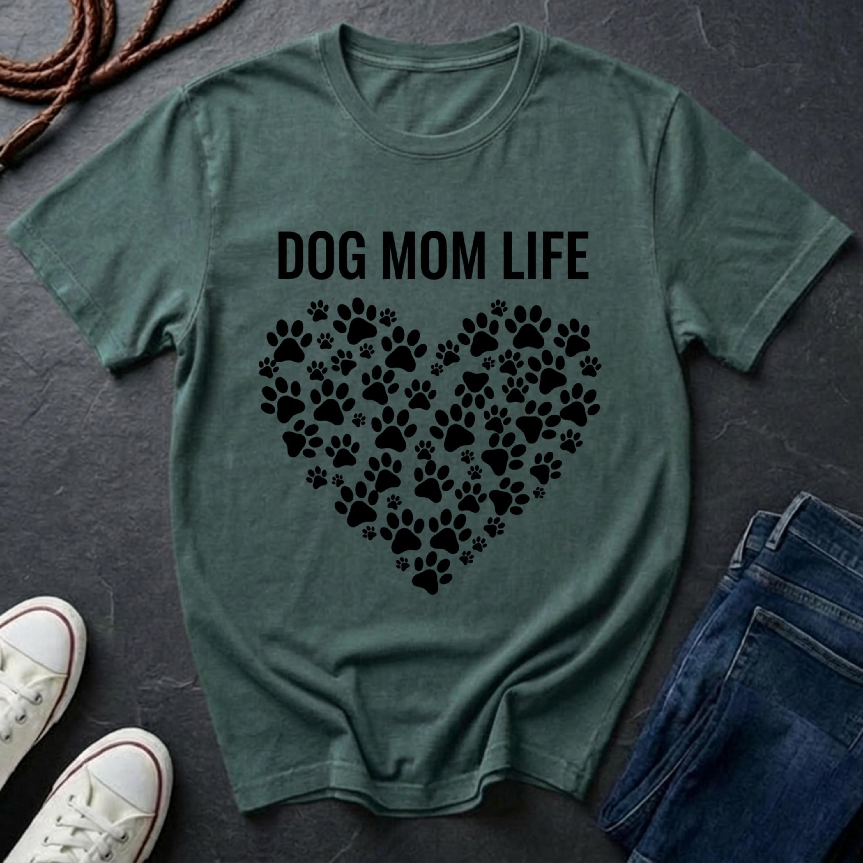 Green Comfort Colors t-shirt with 'DOG MOM LIFE' text and paw prints on a dark surface with shoes and jeans.