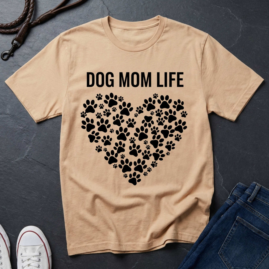 Beige Comfort Colors t-shirt with 'DOG MOM LIFE' text and paw print heart design on a dark surface.