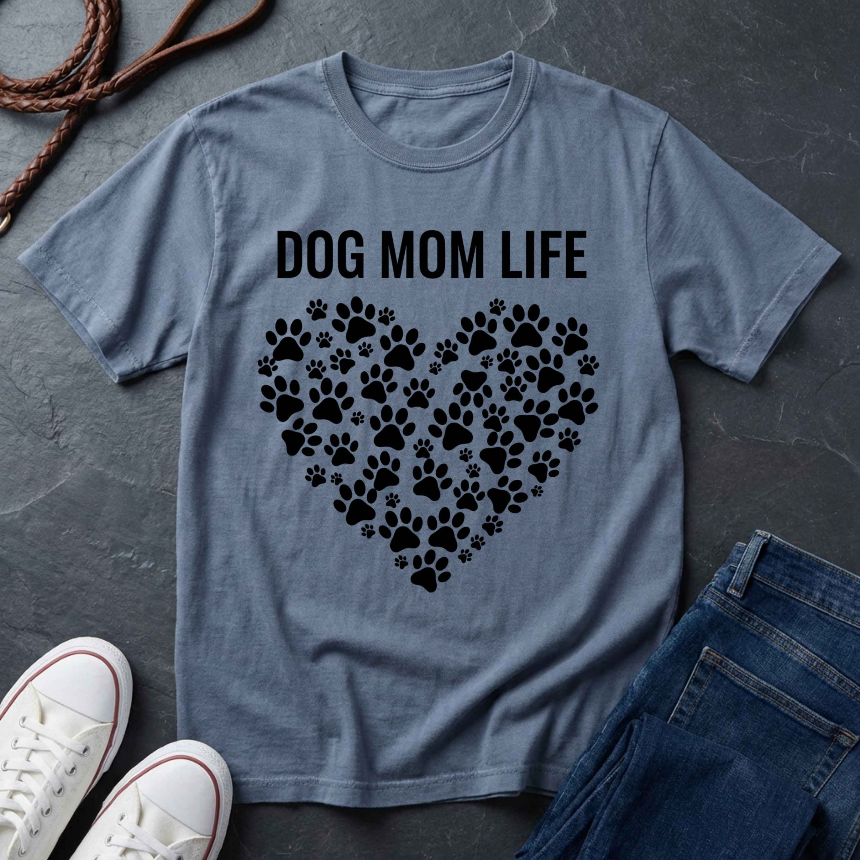 Blue Comfort Colors t-shirt with 'DOG MOM LIFE' text and paw prints on a dark surface with shoes and jeans.