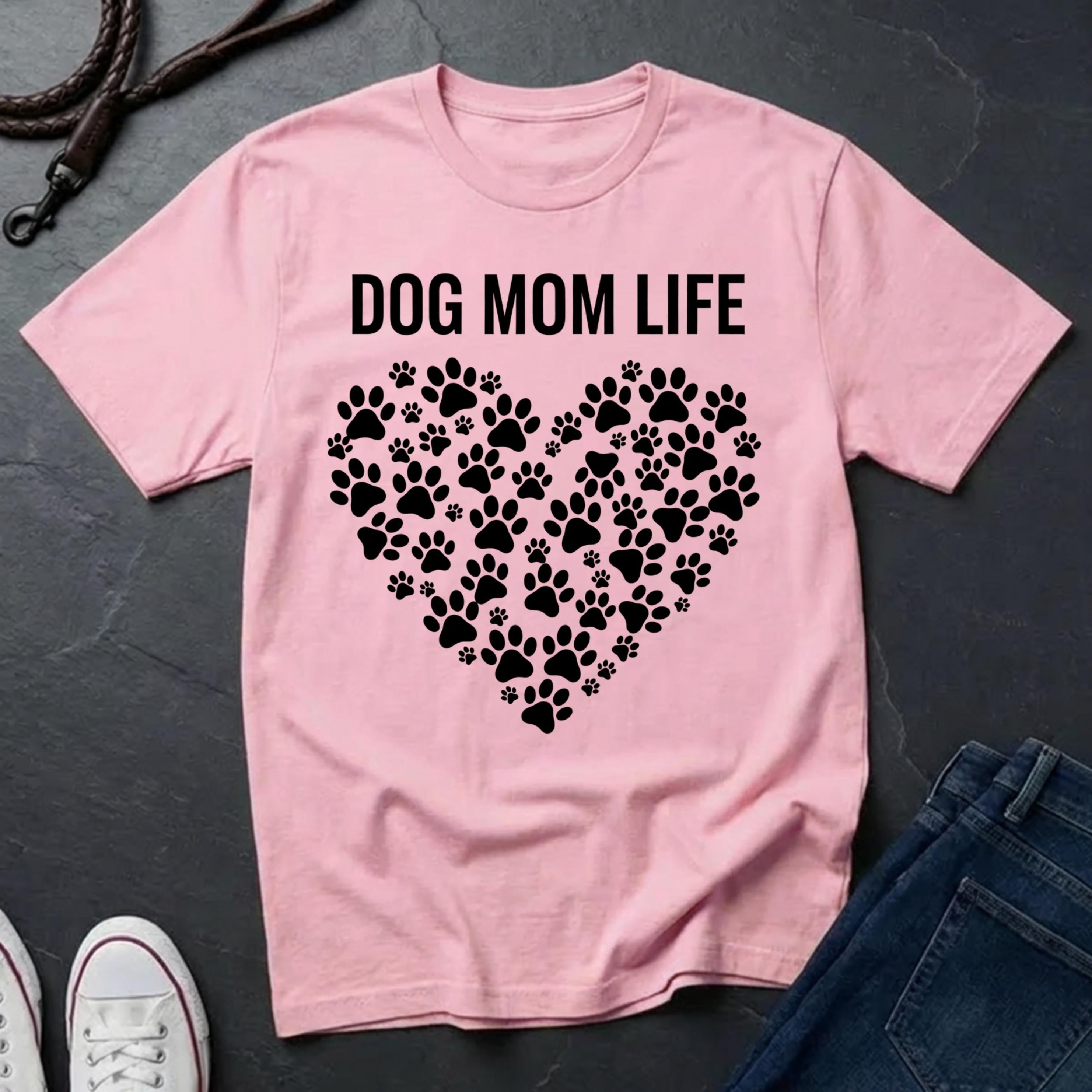 Pink Comfort Colors t-shirt with 'Dog Mom Life' text and paw print design on a dark surface.