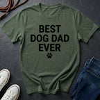 Green Comfort Colors t-shirt with 'Best Dog Dad Ever' text on a dark surface with shoes and jeans.