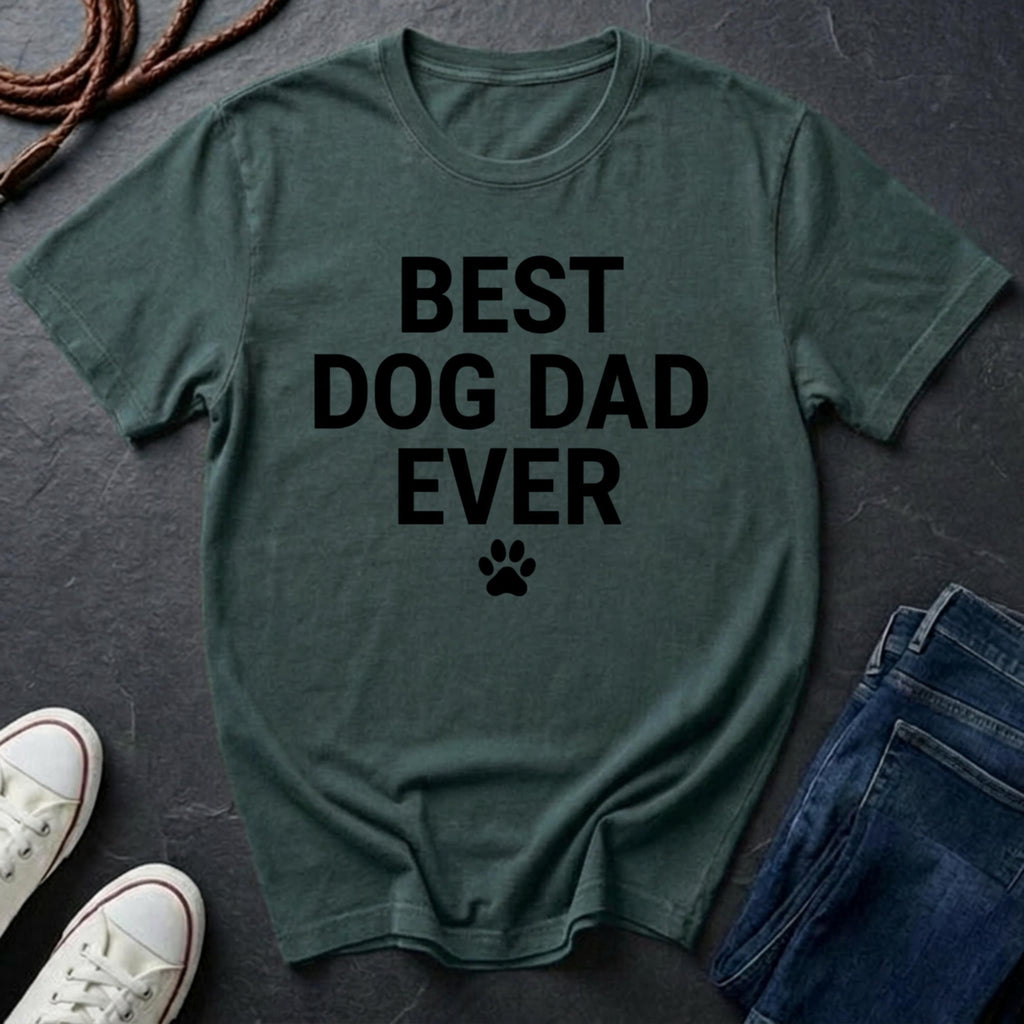 Green Comfort Colors t-shirt with 'BEST DOG DAD EVER' text on a dark surface with shoes and jeans.