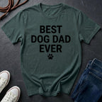 Green Comfort Colors t-shirt with 'BEST DOG DAD EVER' text on a dark surface with shoes and jeans.