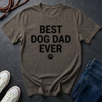 Brown Comfort Colors t-shirt with 'BEST DOG DAD EVER' text on a dark surface with shoes and jeans.