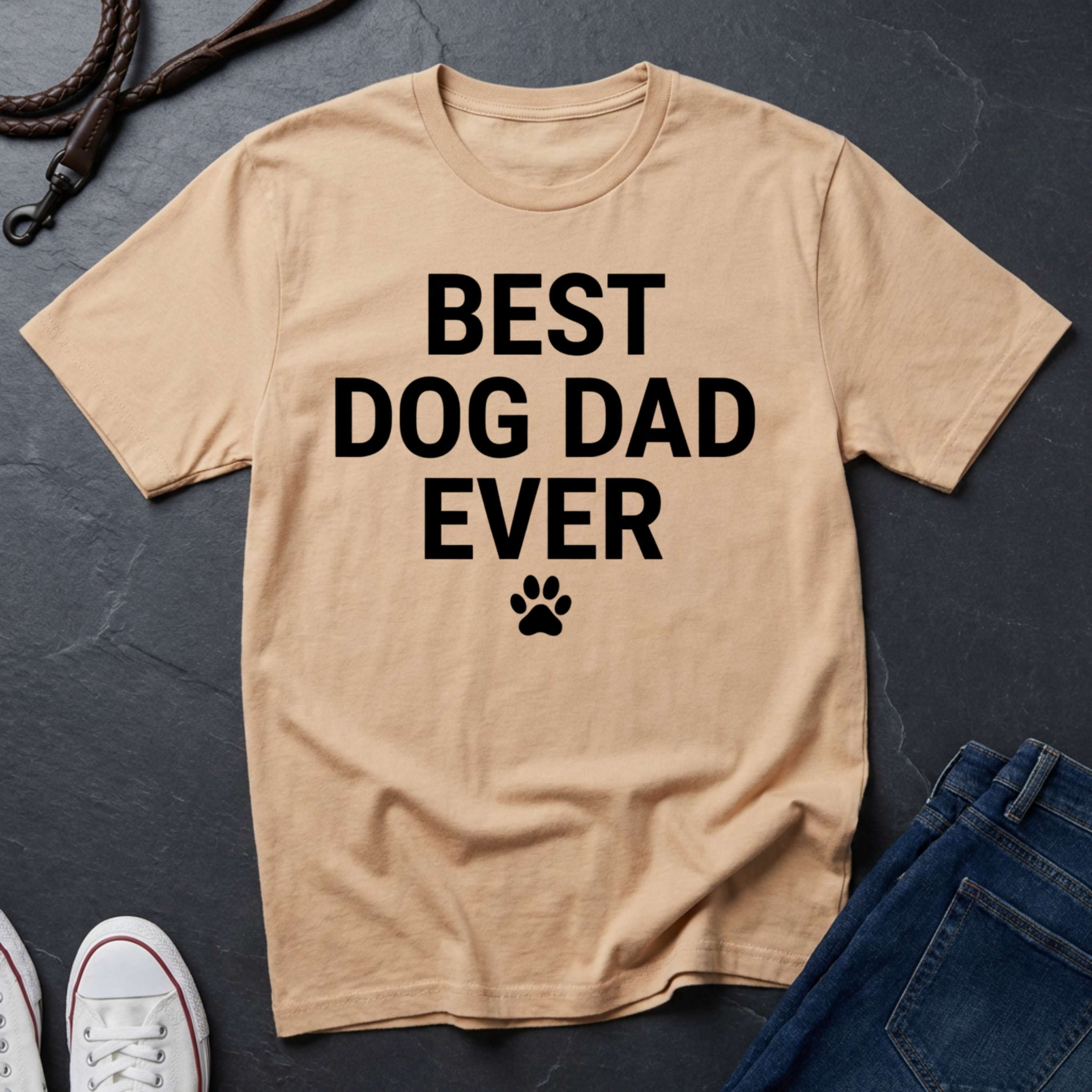 Beige Comfort Colors t-shirt with 'Best Dog Dad Ever' text on a dark surface with jeans and shoes.