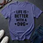 Purple Comfort Colors t-shirt with 'Life is better with a dog' text on a dark surface with shoes and jeans.