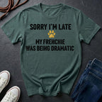Green Comfort Colors t-shirt with text 'Sorry I'm late, my Frenchie was being dramatic' on a dark surface with shoes and jeans.