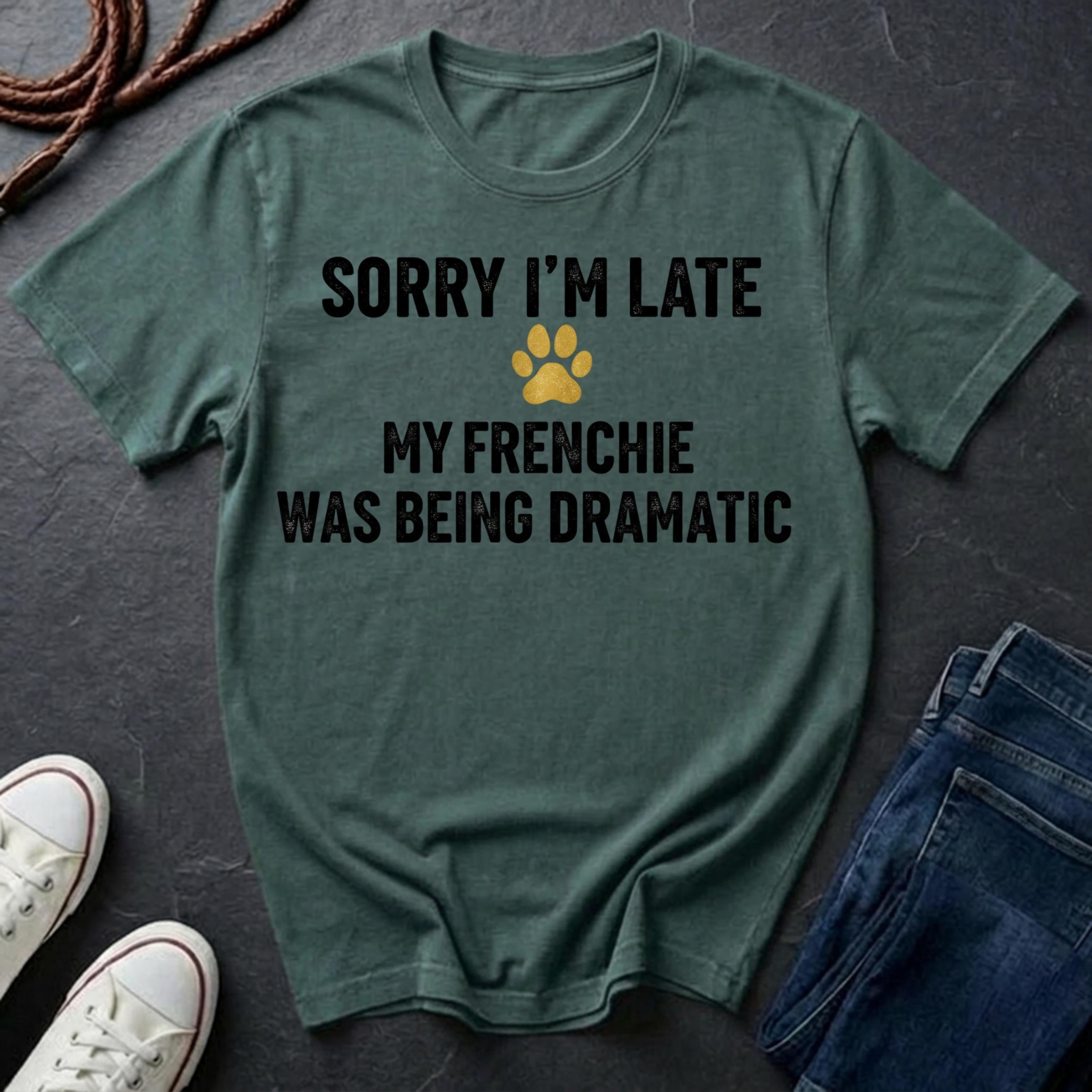 Green Comfort Colors t-shirt with text 'Sorry I'm late, my Frenchie was being dramatic' on a dark surface with shoes and jeans.